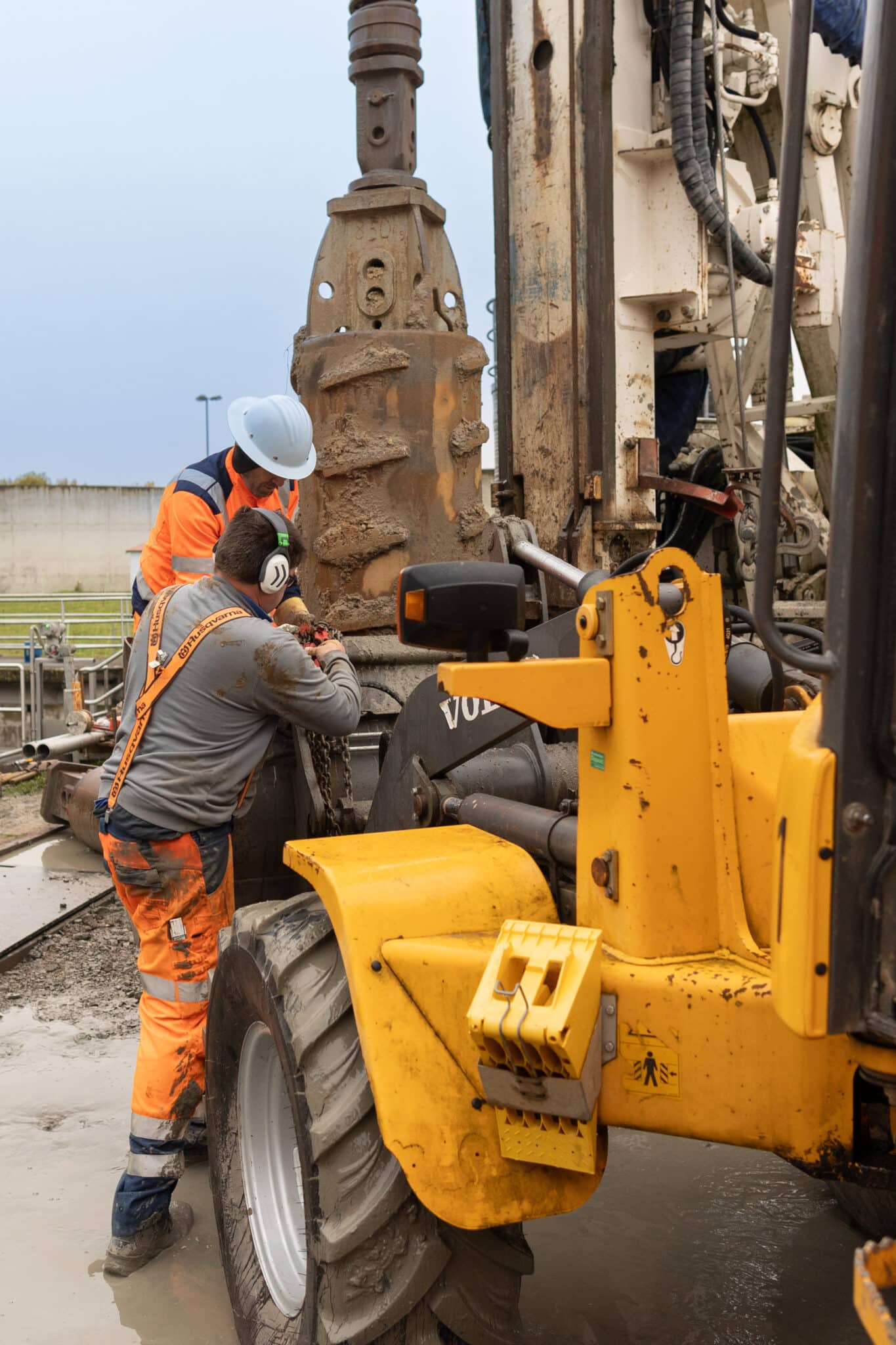 Arbeiter bedienen große Bohrmaschine auf Baustelle.